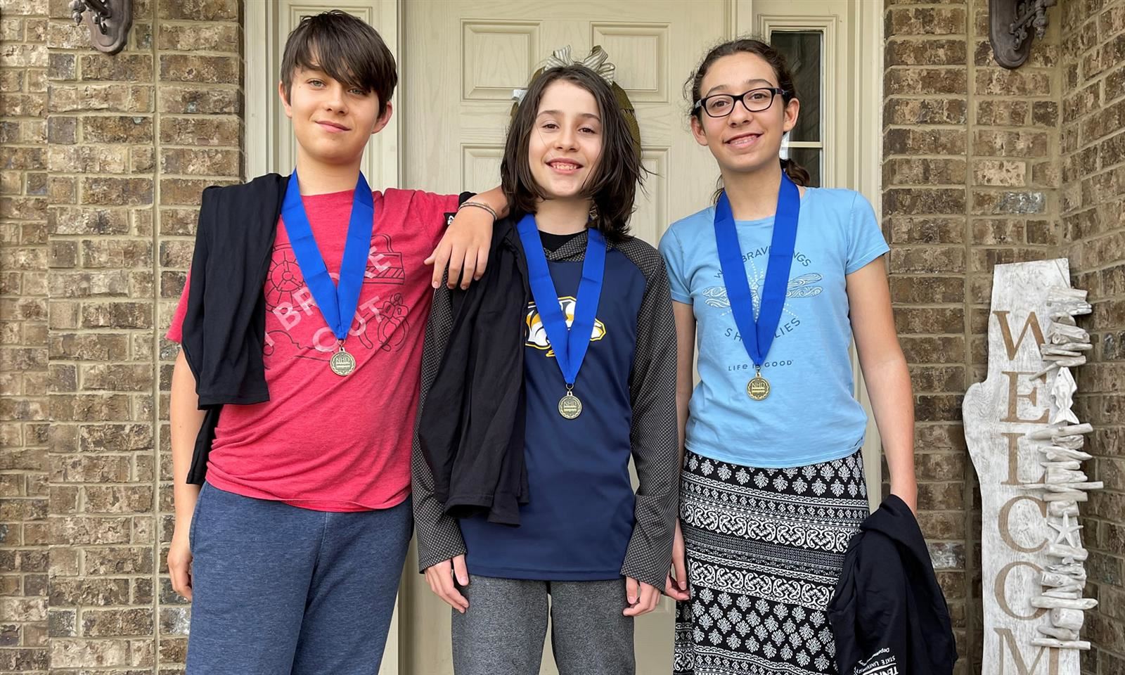 Three students smile while wearing medals